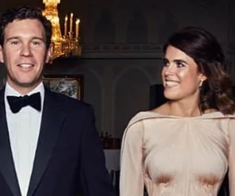 A couple in formal attire, with the woman in a Zac Posen dress, standing in an elegant room with a chandelier.
