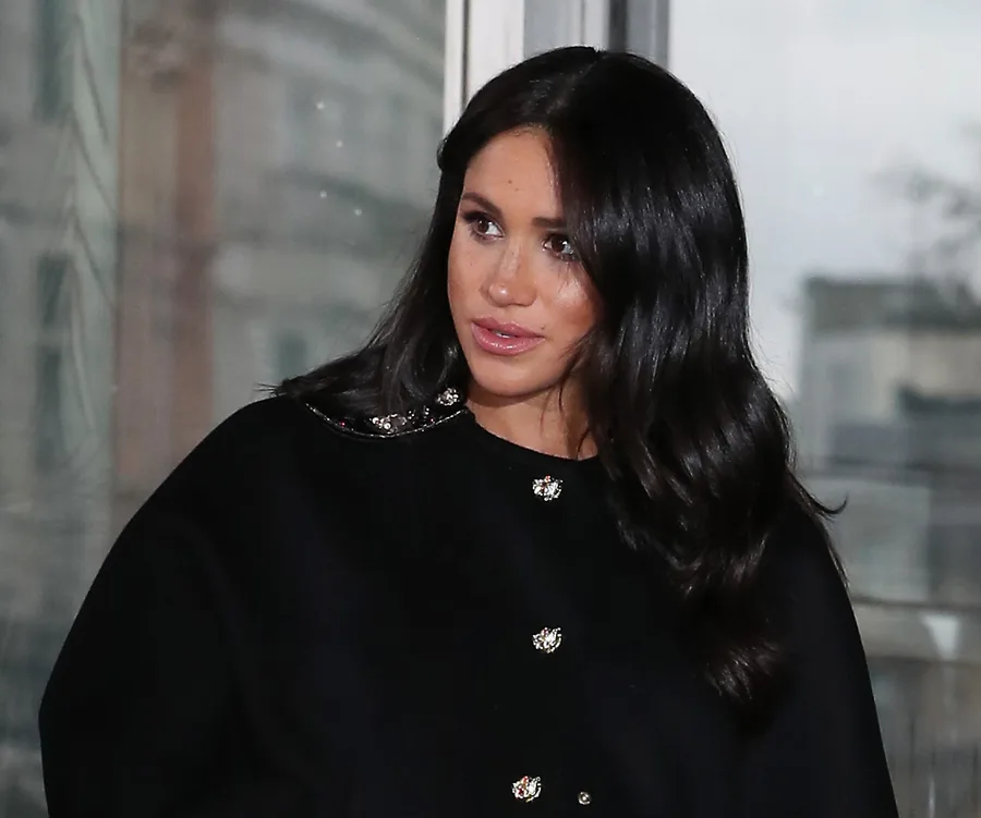 A person with long dark hair wearing a black jacket with decorative buttons, indoors.