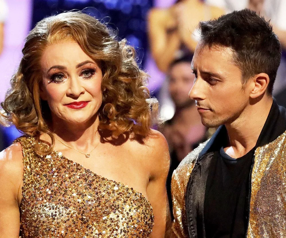 Two Dancing with the Stars contestants in glittery outfits on stage, looking emotional.