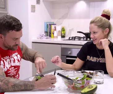 Couple eating together in a modern kitchen setting, smiling and conversing.