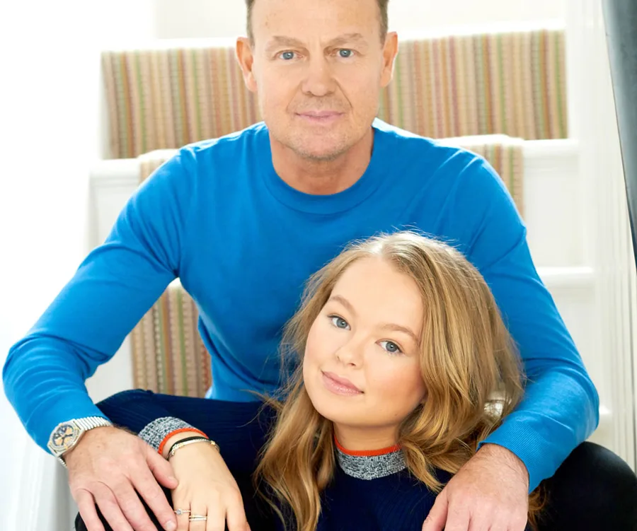 Man in blue shirt with young woman, both smiling, sitting on indoor stairs, close and relaxed.