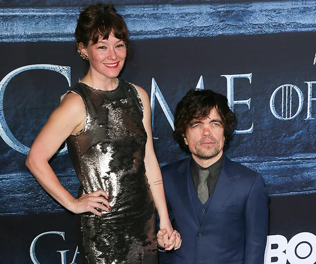 A couple poses at a "Game of Thrones" event, with a woman in a silver dress and a man in a blue suit.