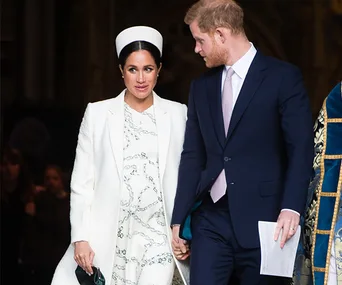Couple walking hand in hand; she is wearing a white outfit and hat, and he is in a suit with a pink tie.