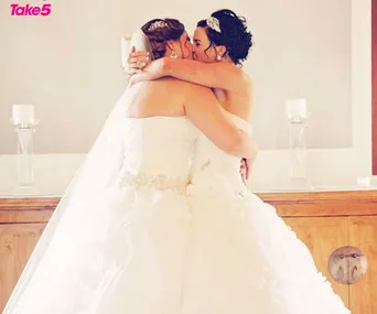 Two brides in white dresses share a kiss, embracing each other at their wedding ceremony.