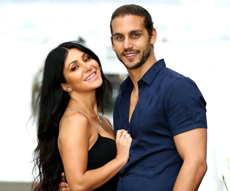Couple embracing and smiling at the camera against a blurred outdoor background.