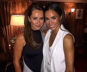 Two women smiling and posing in a warmly lit room.