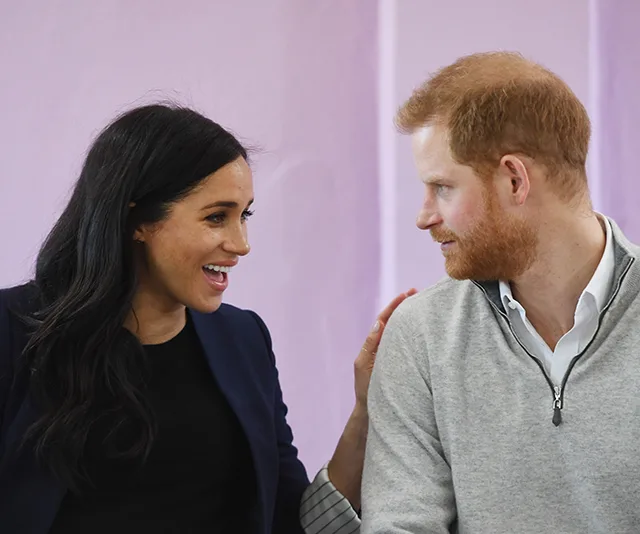 Couple smiling and talking, seated, with a soft pink background.