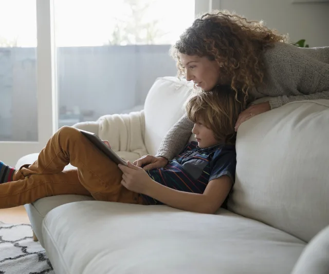 Mother and child on a sofa, looking at a tablet together.