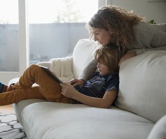 Mother and child on a sofa, looking at a tablet together.