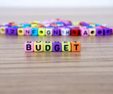 Colorful letter cubes spelling "BUDGET" on a wooden surface with scattered cubes in the background.