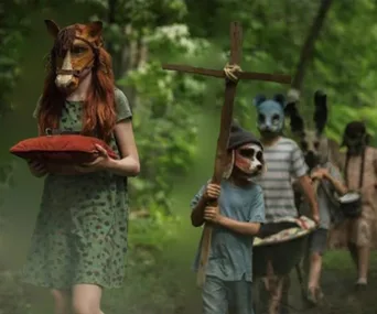 Children wearing animal masks walk through the woods, one with a cross, in a scene from "Pet Sematary" film.