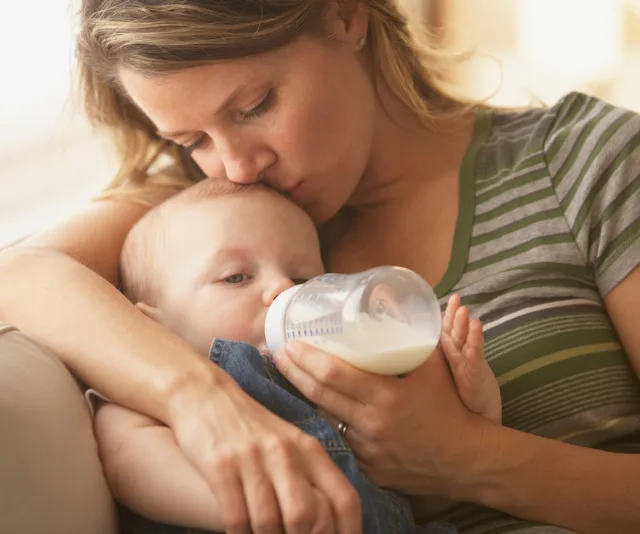 Mother cradles and feeds baby with a bottle while kissing baby's head.