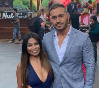 A woman in a blue dress and a man in a gray suit pose together outdoors.