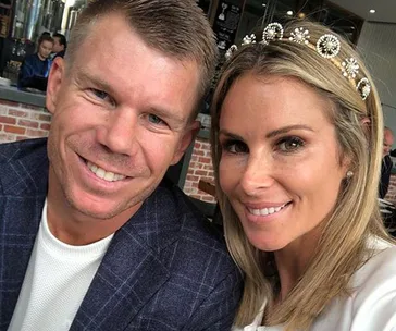 A couple smiling for a selfie in a cafe, with the woman wearing a jeweled headband.