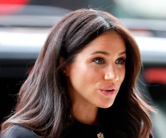 A woman with long dark hair, wearing a dark outfit, looks to the side with a soft expression.