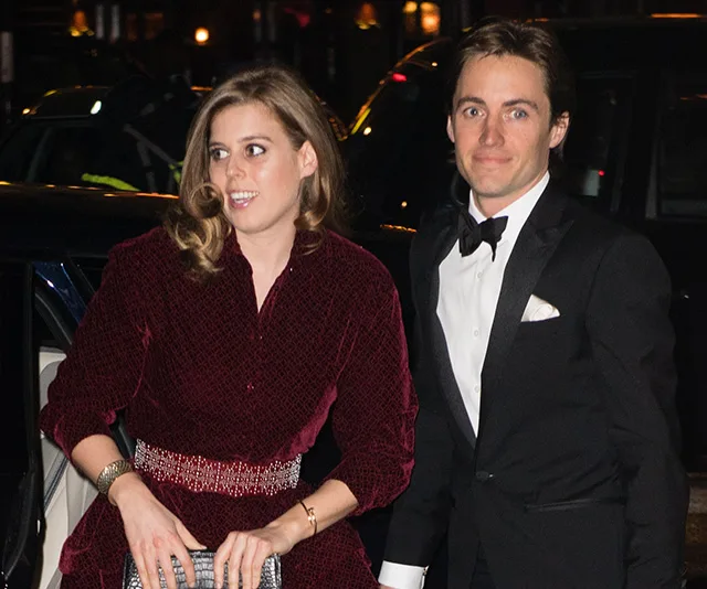 A couple dressed elegantly at night, with the woman in a dark dress and man in a tuxedo, standing by a car.