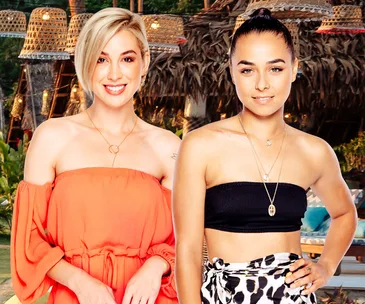 ALT text: Two women smiling, one in an orange off-shoulder dress and the other in a black crop top, with a tropical background.