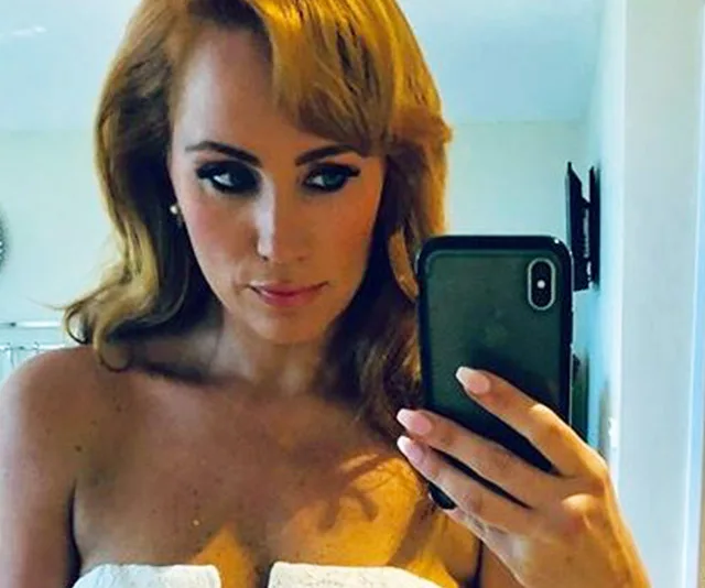 Woman taking a selfie in a strapless outfit, holding a smartphone in front of a mirror.