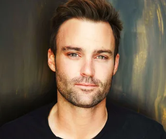 Portrait of a man with short hair and a beard, wearing a dark shirt against a blurred background.