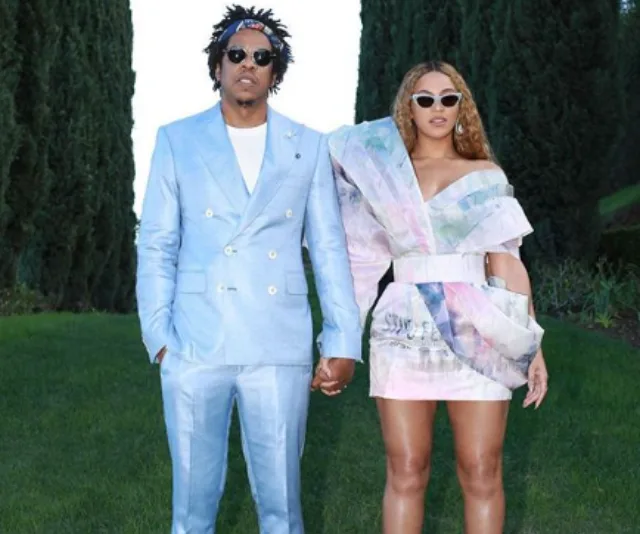 A couple in stylish outfits holding hands; the man in a blue suit and the woman in a colorful mini dress with sunglasses.