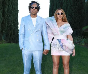 A couple in stylish outfits holding hands; the man in a blue suit and the woman in a colorful mini dress with sunglasses.