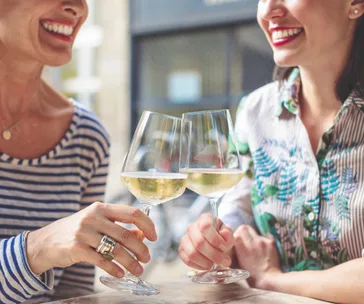 Two people smiling and clinking wine glasses at a cafe.