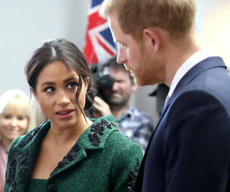 A woman in a green coat and a man in a suit are engaged in conversation with a Union Jack flag in the background.