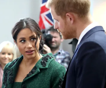 A woman in a green coat and a man in a suit are engaged in conversation with a Union Jack flag in the background.