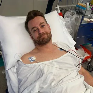 Man in a hospital bed with medical sensors on his chest and a relaxed expression.
