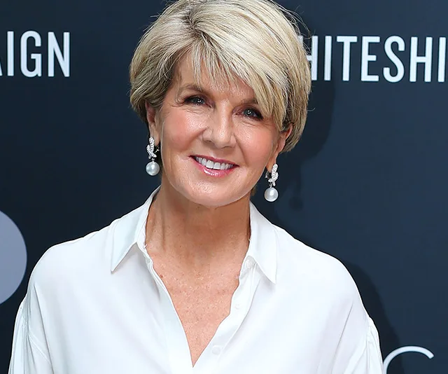 Woman in a white shirt smiling with pearl earrings against a dark background.