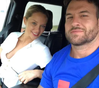 A couple sitting in a car, both smiling, the man wearing a blue t-shirt and the woman in a white top.