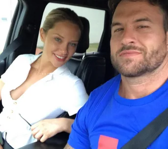 A couple sitting in a car, both smiling, the man wearing a blue t-shirt and the woman in a white top.