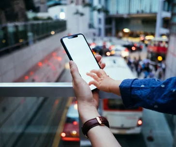 Adult and child's hand holding a smartphone with a busy city street background.
