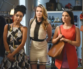 Three women stand in a fashion store, each dressed stylishly, with handbags and clothing displayed in the background.
