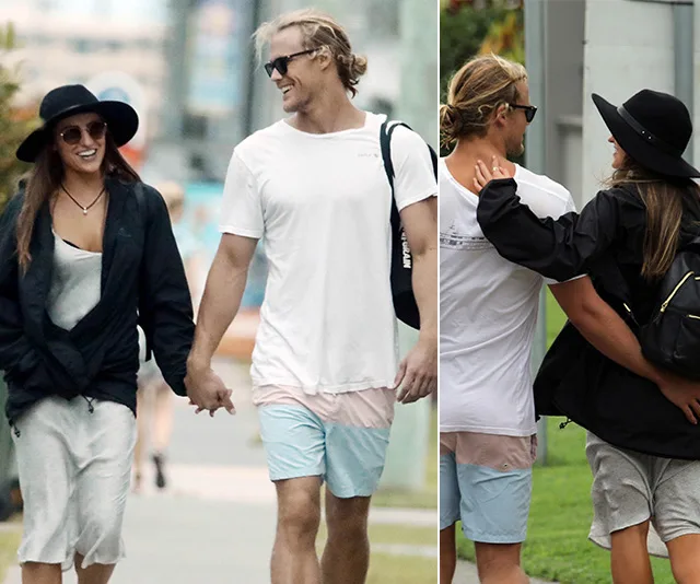 Couple smiling and holding hands while walking outdoors, wearing casual summer outfits and sunglasses.
