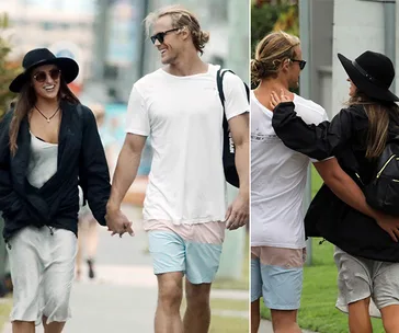 Couple smiling and holding hands while walking outdoors, wearing casual summer outfits and sunglasses.