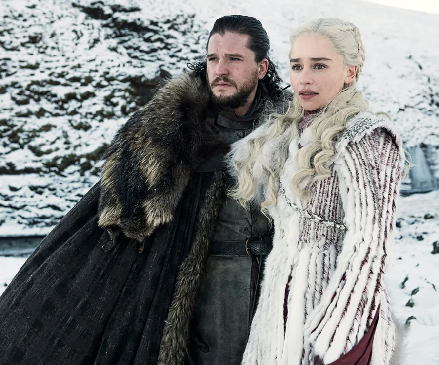 Two characters from "Game of Thrones" stand in a snowy landscape, dressed in winter attire.