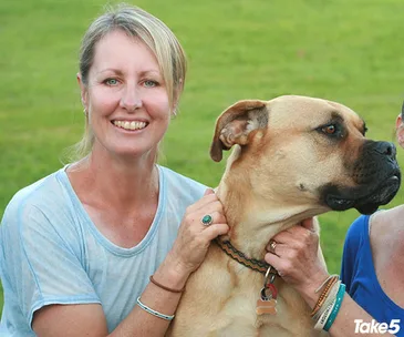 ```html
A woman smiling while holding a large brown dog outside on a grassy field.
```