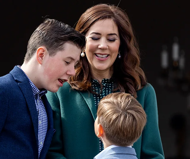 "Smiling woman in green coat with two boys outdoors, enjoying a conversation."