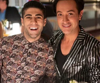 Two men smiling at a party, one wearing a paisley shirt, the other a glittery striped jacket.