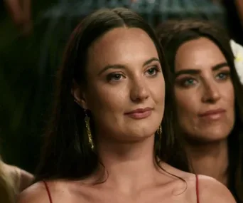 Female contestants seated attentively on a reality show set.