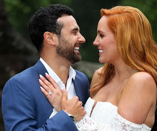 A couple smiling lovingly at each other during their engagement party, showcasing the woman's engagement ring.