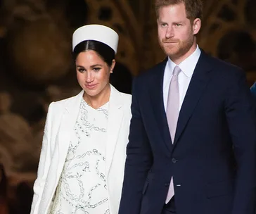 Couple walking together, with the woman in a white outfit and the man in a suit, looking ahead.