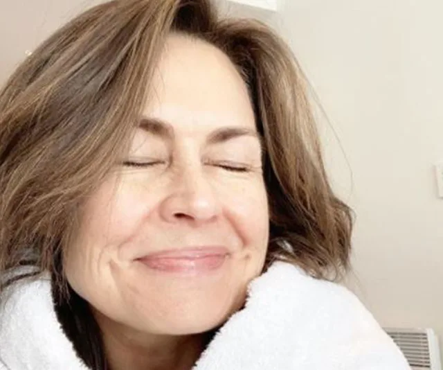 A woman with brown hair smiling, eyes closed, wearing a white robe, with a calm expression.