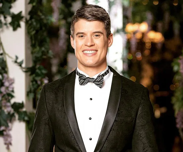 Man smiling in a tuxedo in front of a floral backdrop.