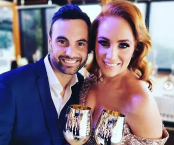 A couple smiling and holding metallic goblets, dressed in formal attire at an event.