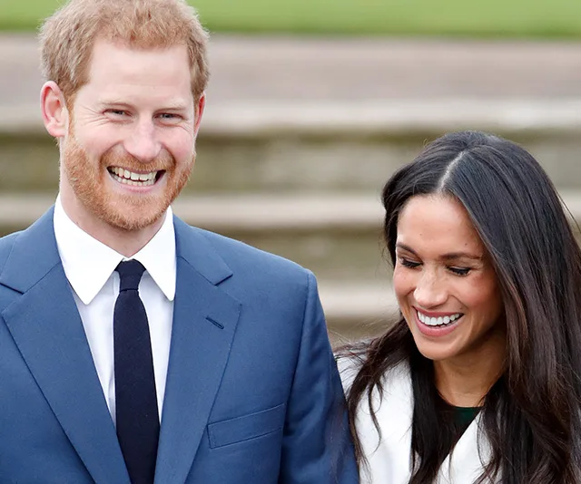 A smiling couple in formal attire walk together outside with stairs in the background.