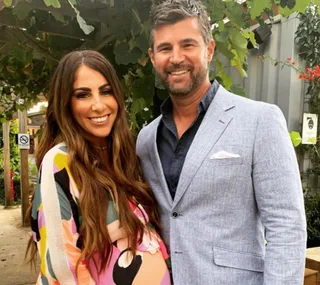 Man in a light blue suit and woman in a colorful dress smiling, standing in an outdoor setting.