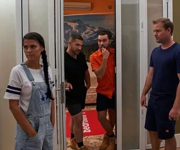 Four people inside a room: a woman in overalls with a braid and three men, two standing in a doorway, one in blue nearby.