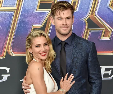 Couple smiling on a red carpet event with a movie poster in the background.